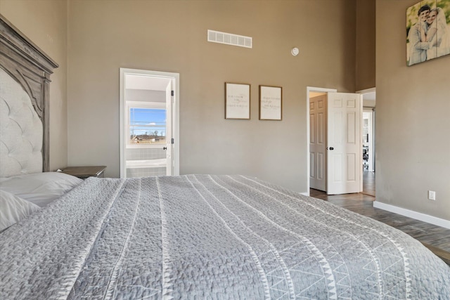 bedroom featuring wood finished floors, visible vents, baseboards, a towering ceiling, and connected bathroom