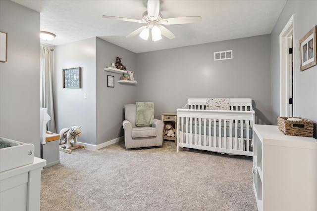 carpeted bedroom with visible vents, baseboards, a nursery area, and ceiling fan