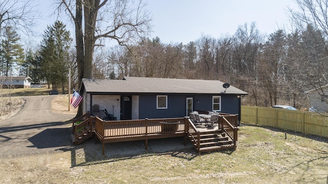 rear view of property with a deck, concrete driveway, fence, and a shingled roof