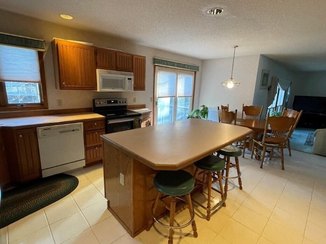 kitchen with brown cabinetry, hanging light fixtures, white appliances, and a center island