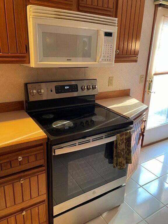 kitchen with light tile patterned floors, white microwave, light countertops, stainless steel range with electric stovetop, and brown cabinets