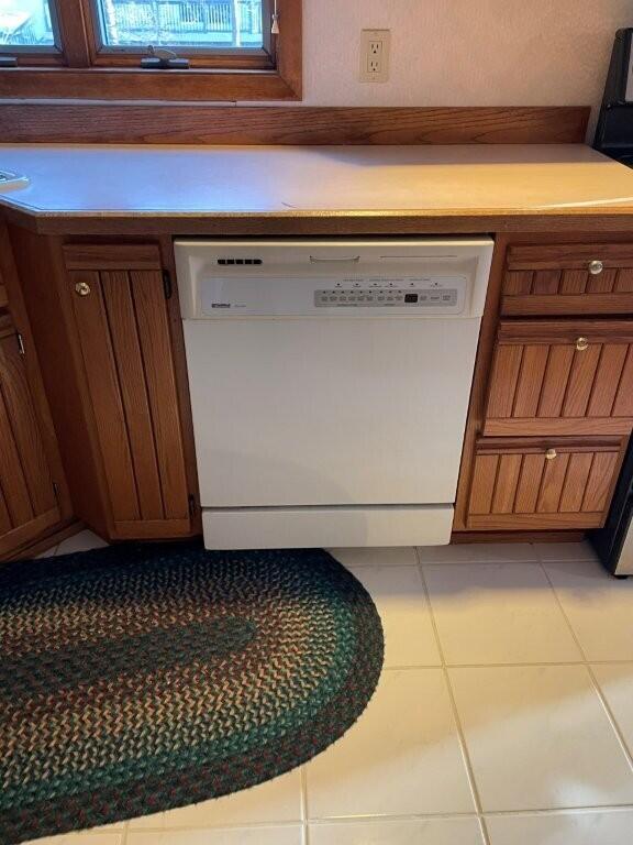 interior space featuring dishwasher, light countertops, light tile patterned floors, and brown cabinetry