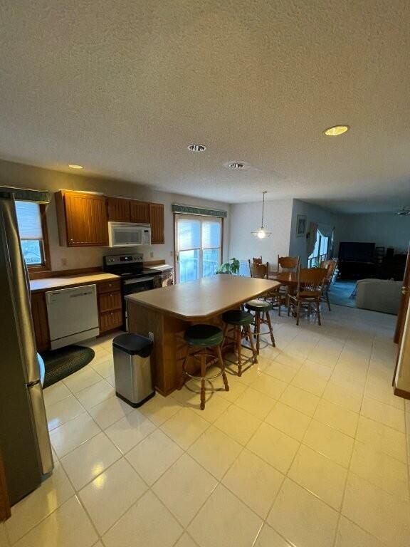 kitchen with a center island, a breakfast bar area, appliances with stainless steel finishes, brown cabinetry, and a textured ceiling