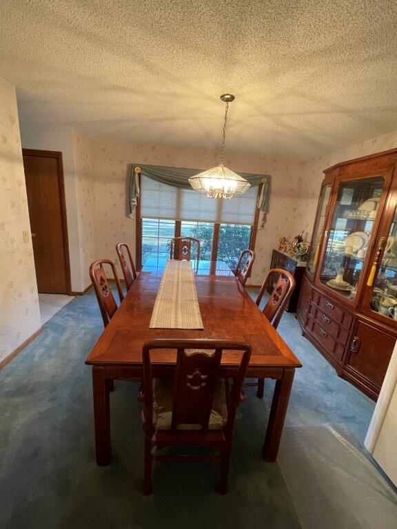 dining area with a notable chandelier, carpet flooring, wallpapered walls, and a textured ceiling