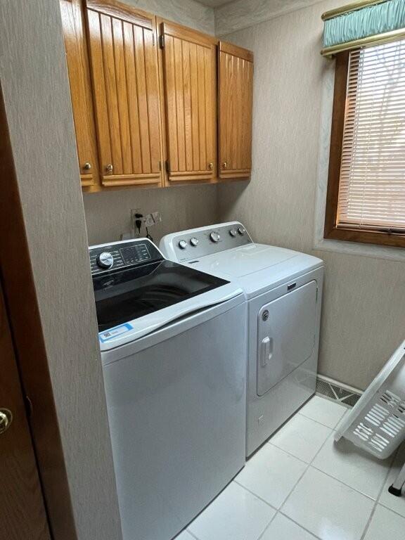 laundry area featuring light tile patterned floors, cabinet space, a textured wall, and washing machine and clothes dryer