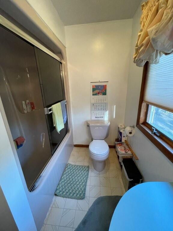 bathroom with toilet, baseboards, and shower / bath combination with glass door