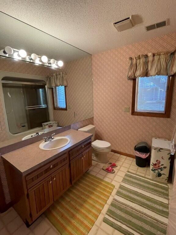 bathroom featuring wallpapered walls, vanity, visible vents, and a textured ceiling