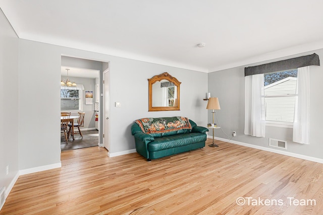 living area featuring a chandelier, visible vents, baseboards, and wood finished floors