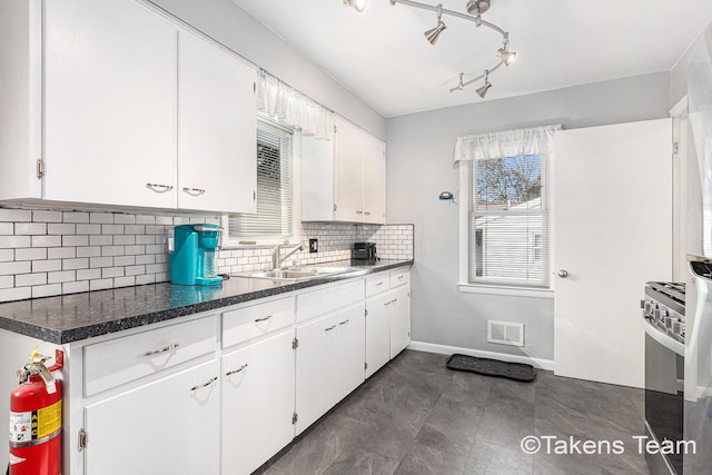 kitchen featuring dark countertops, backsplash, white cabinets, and a sink