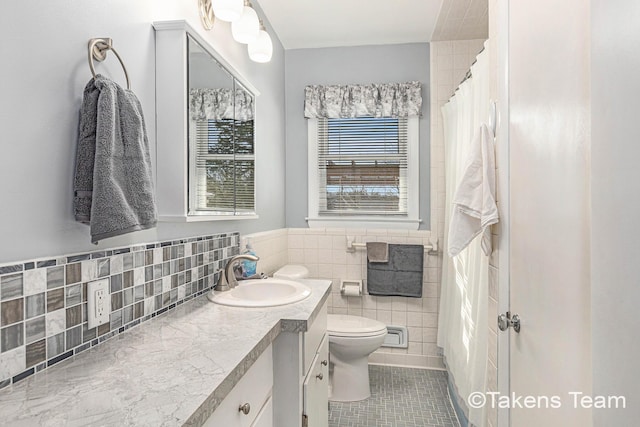 bathroom with tile patterned flooring, a wainscoted wall, toilet, vanity, and tile walls