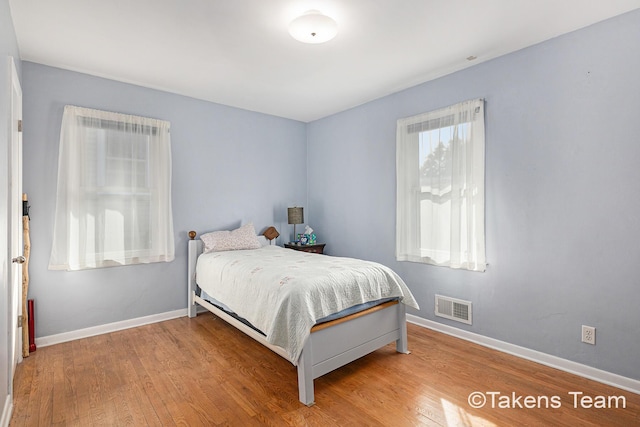 bedroom with wood finished floors, visible vents, and baseboards