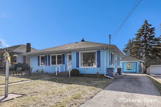 bungalow-style house with an outbuilding, concrete driveway, a front yard, and roof with shingles