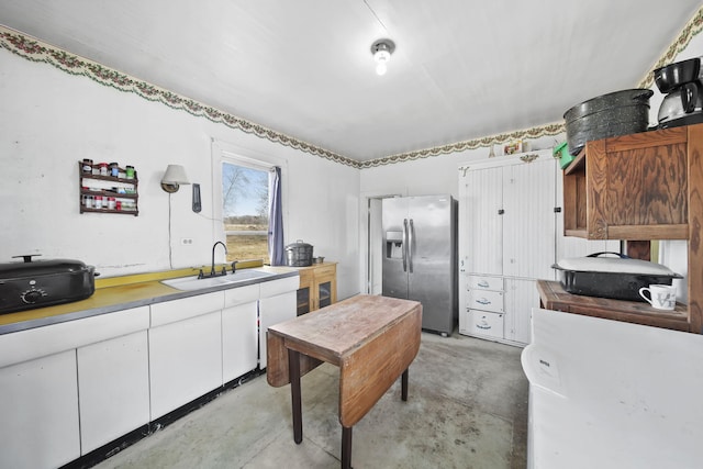 kitchen featuring white cabinets, stainless steel fridge, concrete flooring, and a sink