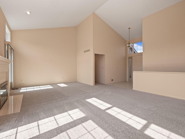 unfurnished room featuring visible vents, a fireplace with flush hearth, high vaulted ceiling, baseboards, and light colored carpet