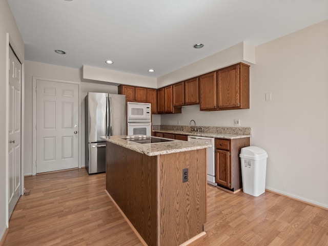 kitchen featuring recessed lighting, light wood-type flooring, white appliances, and light stone countertops