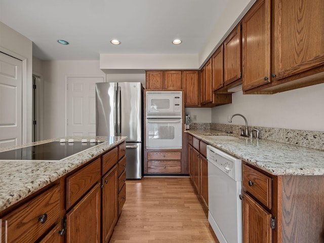 kitchen with recessed lighting, light wood-style flooring, brown cabinetry, white appliances, and a sink