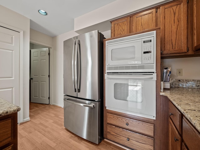 kitchen featuring brown cabinetry, white appliances, light wood-style floors, and light stone countertops