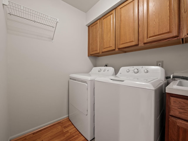 clothes washing area with separate washer and dryer, light wood-style flooring, cabinet space, and baseboards