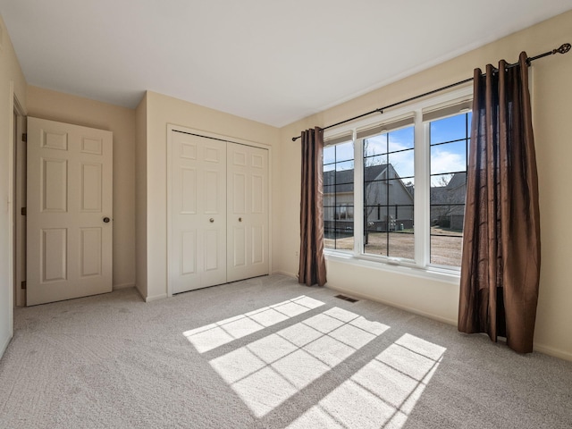 unfurnished bedroom with a closet, light carpet, baseboards, and visible vents