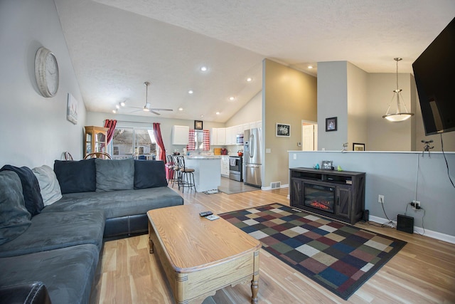 living room with light wood-style flooring, a ceiling fan, a textured ceiling, baseboards, and vaulted ceiling