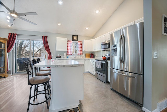 kitchen with ceiling fan, vaulted ceiling, appliances with stainless steel finishes, white cabinetry, and a center island