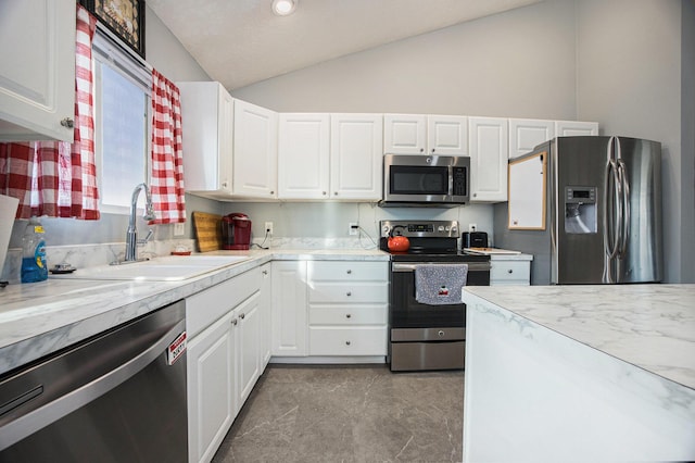 kitchen with white cabinets, appliances with stainless steel finishes, lofted ceiling, and a sink