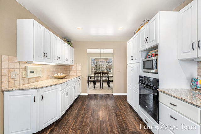 kitchen featuring dark wood-type flooring, white cabinets, stainless steel microwave, black oven, and backsplash