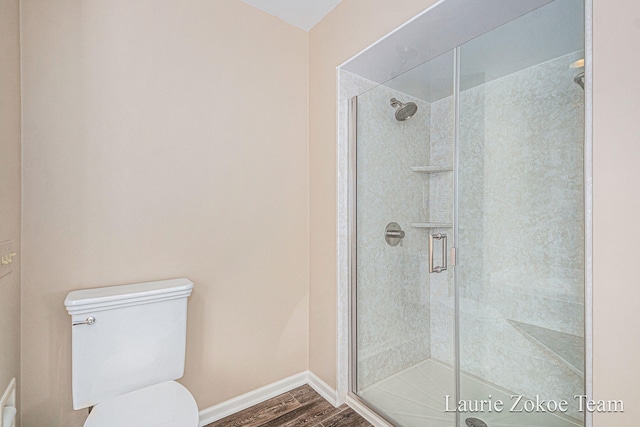 full bath featuring baseboards, toilet, wood finished floors, and a shower stall