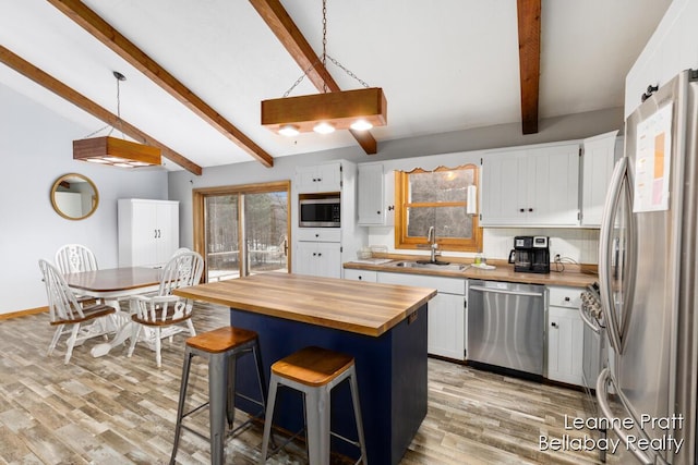 kitchen featuring vaulted ceiling with beams, a sink, white cabinets, appliances with stainless steel finishes, and butcher block counters