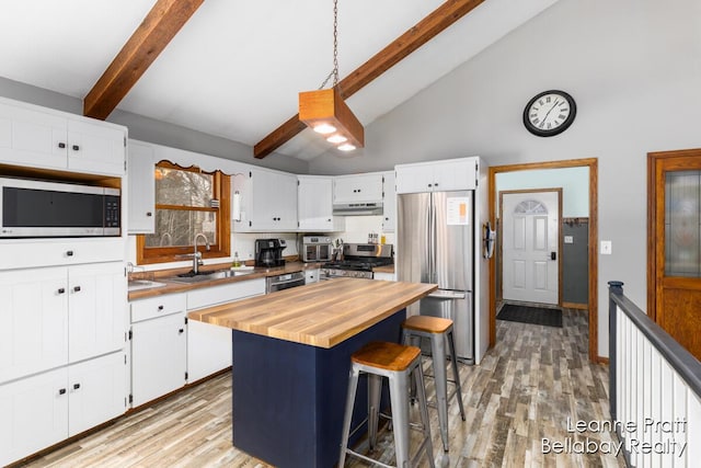 kitchen with under cabinet range hood, butcher block countertops, light wood-style flooring, appliances with stainless steel finishes, and a sink