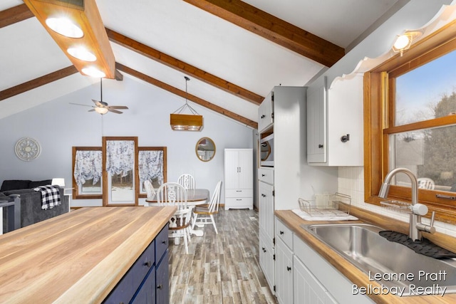 kitchen with blue cabinetry, butcher block countertops, light wood-style floors, white cabinets, and a sink