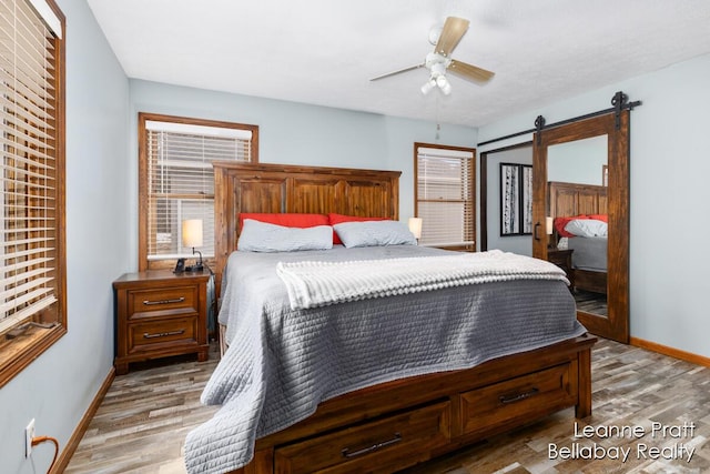 bedroom with a barn door, baseboards, light wood finished floors, and ceiling fan