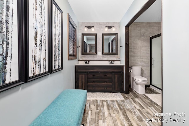 full bathroom featuring toilet, double vanity, wood finished floors, tile walls, and a sink