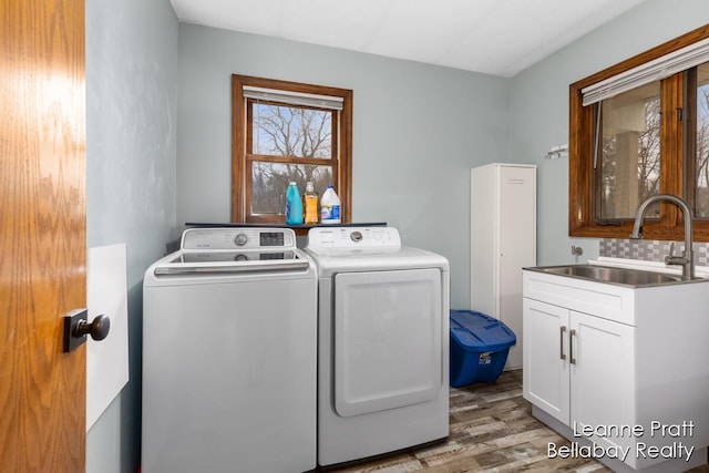 clothes washing area featuring washer and clothes dryer, wood finished floors, cabinet space, and a sink