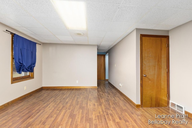 unfurnished room featuring a paneled ceiling, wood finished floors, visible vents, and baseboards