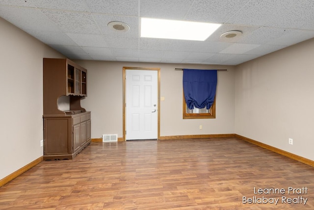 unfurnished living room featuring light wood-type flooring, visible vents, baseboards, and a paneled ceiling