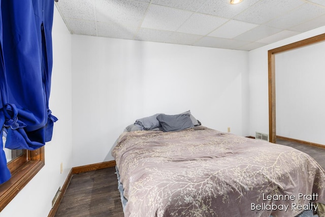 bedroom featuring a paneled ceiling, visible vents, baseboards, and wood finished floors