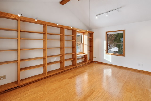 spare room with lofted ceiling with beams, light wood-style flooring, baseboards, and track lighting