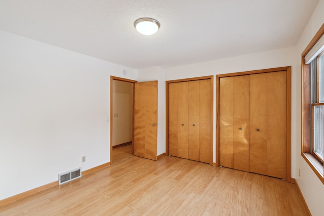 unfurnished bedroom featuring visible vents, multiple closets, baseboards, and light wood finished floors