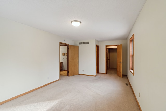 unfurnished bedroom featuring visible vents, a walk in closet, baseboards, light carpet, and ensuite bath