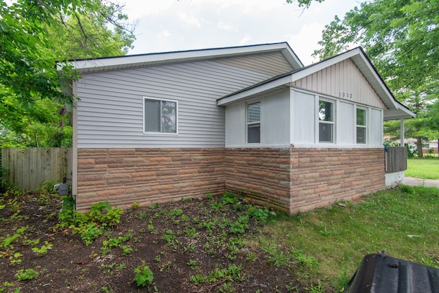 view of side of home with stone siding and fence