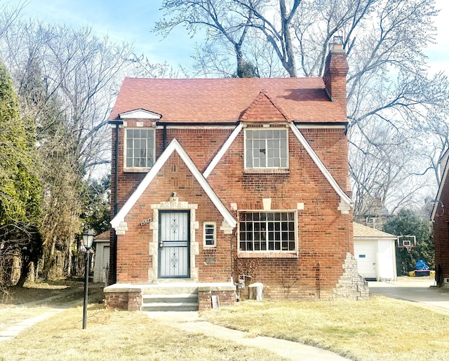 tudor-style house with a shingled roof, brick siding, and a chimney