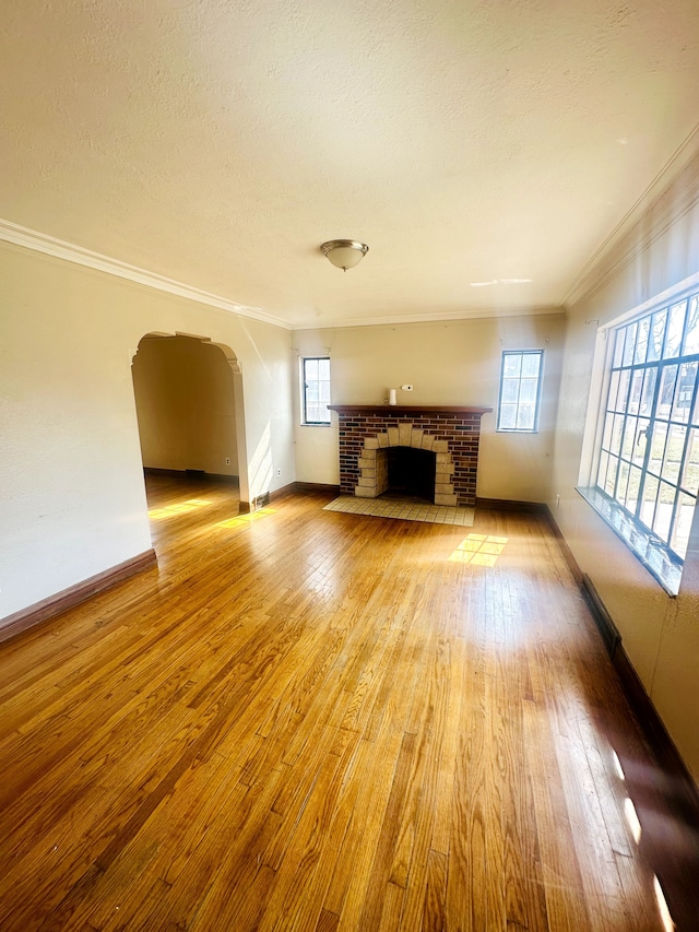 unfurnished living room featuring a fireplace, arched walkways, hardwood / wood-style flooring, a textured ceiling, and crown molding