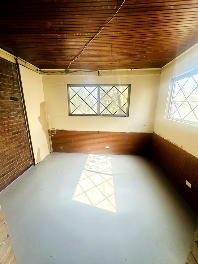 empty room with wood ceiling, finished concrete floors, and brick wall