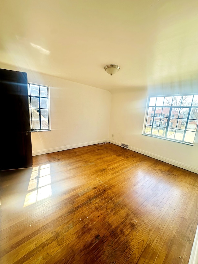 spare room with hardwood / wood-style floors, visible vents, and baseboards