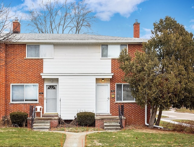 view of front of home with entry steps, a front yard, brick siding, and a chimney