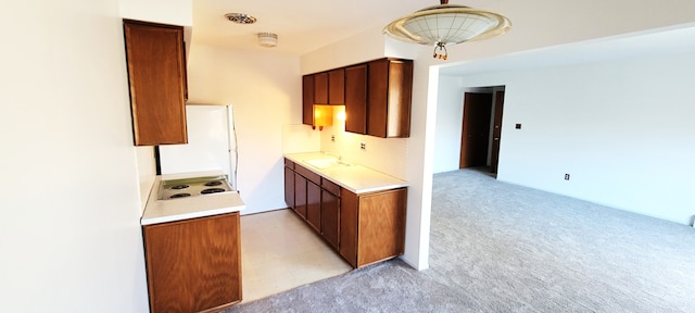 kitchen featuring light countertops, brown cabinets, freestanding refrigerator, and light carpet