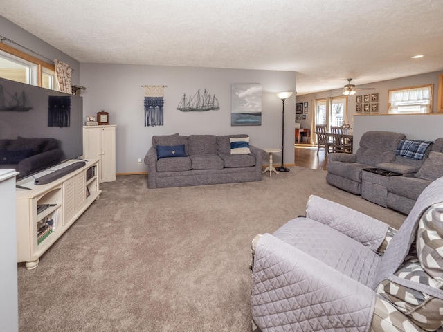 living room featuring ceiling fan, light carpet, and a textured ceiling