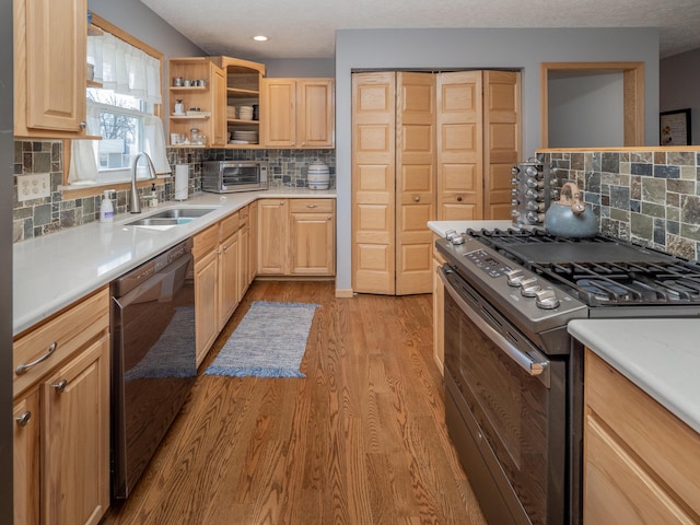 kitchen with light wood finished floors, light brown cabinetry, dishwasher, stainless steel gas range, and a sink