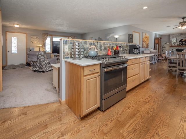 kitchen featuring decorative backsplash, stainless steel gas stove, ceiling fan, and light brown cabinets